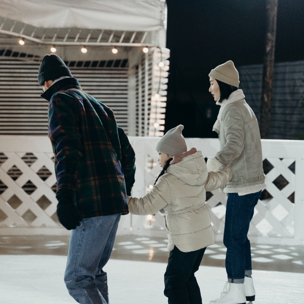family skating on outdoor ice rink with white fence around it