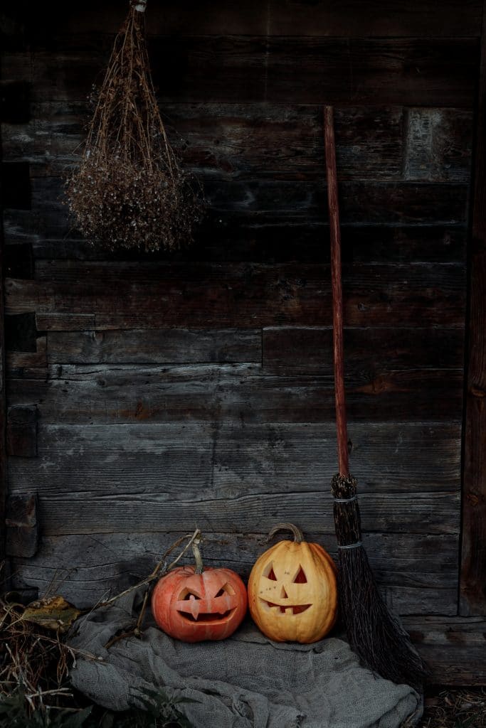black shiplap boarded room with a witches broom and two carved pumpkins.