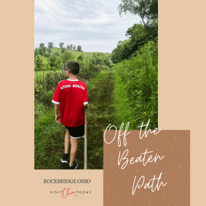 rockbridge ohio feature image. Boy with red shirt, black shorts and walking stick walking away from the camera on a hike with green bushes and trees all around