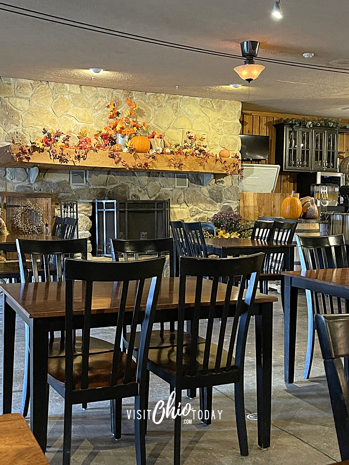 vertical photo of the inside of spring hill winery. black chairs and wooden tables, pumpkin and straw fall decor on stone fireplace Photo credit: Cindy Gordon of VisitOhioToday.com