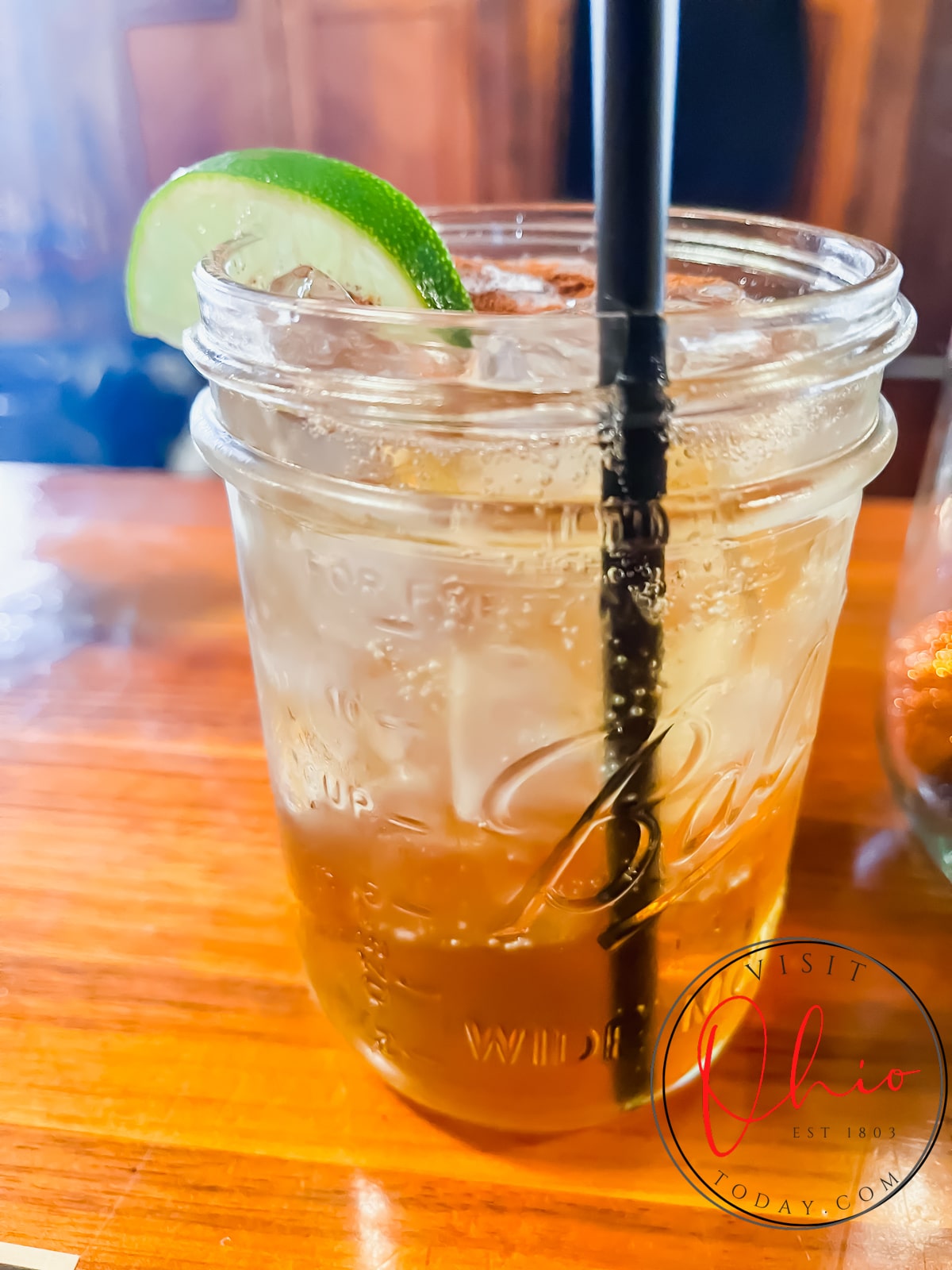 mason jar filled with ice, clear liquid and brown liquid with a black straw and a slice of lime Photo credit: Cindy Gordon of VisitOhioToday.com