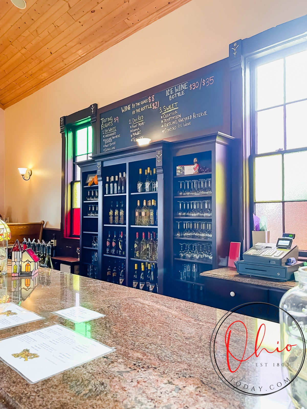 Vertical photo of a wine display with a chalkboard above it, and a bar in the foreground, at South River Winery. Photo credit: Cindy Gordon of VisitOhioToday.com