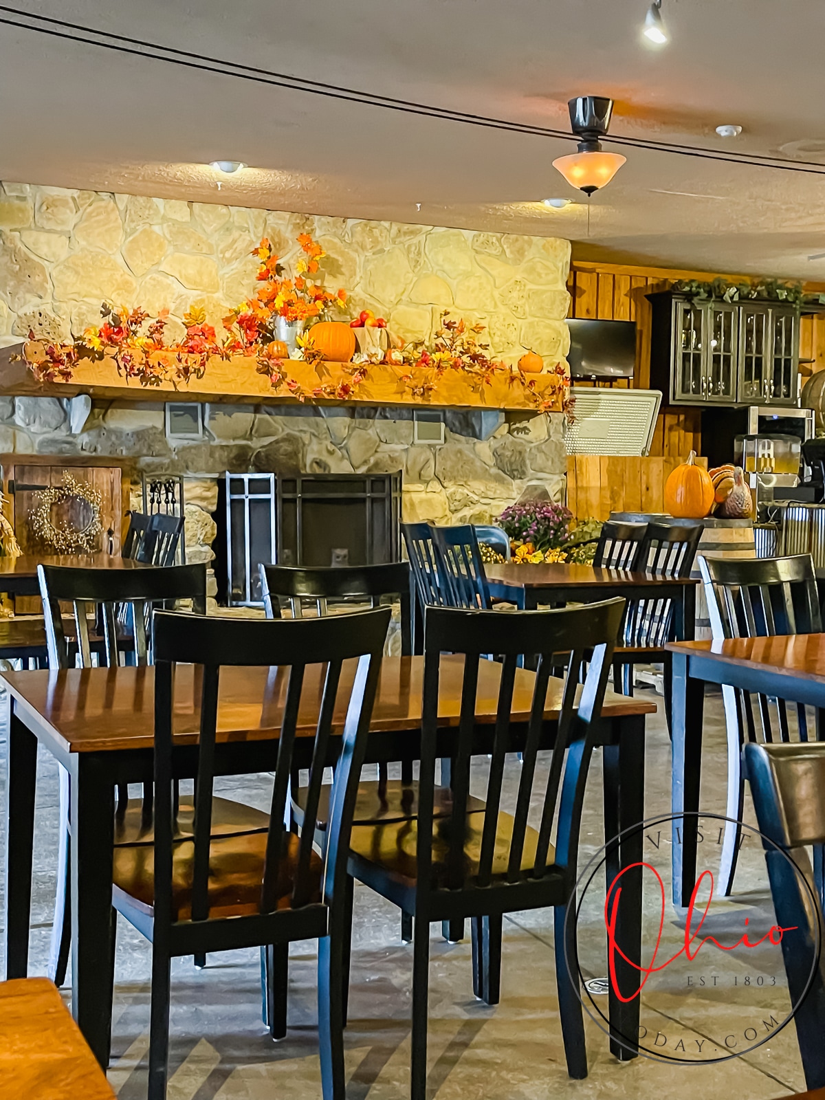Picture of the inside of spring hill winery. black chairs and wooden tables, pumpkin and straw fall decor on stone fireplace