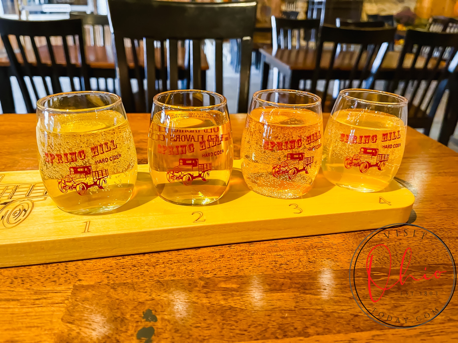 4 small glasses of spring hill winery ciders on a wooden board