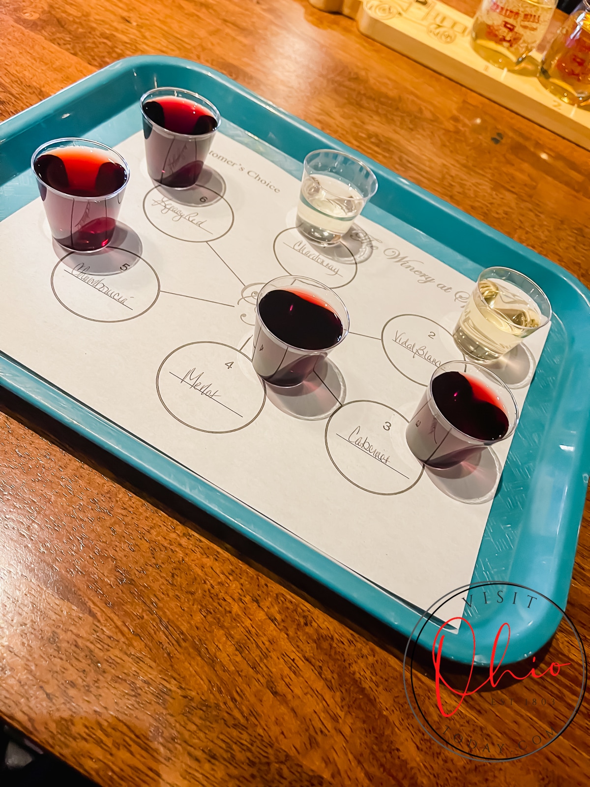 blue tray with a white paper with writing and plastic shot glasses filled with wine