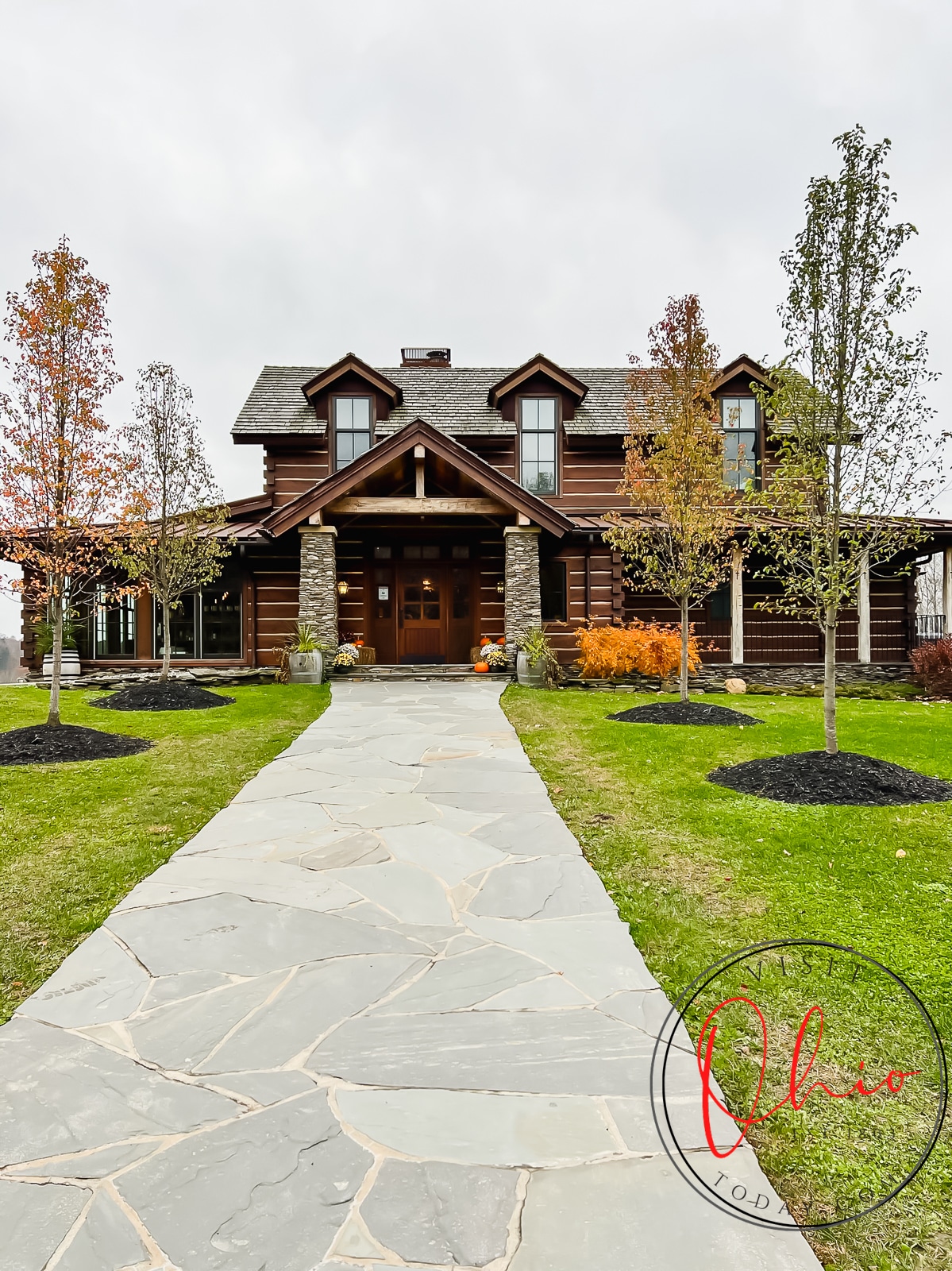 pictured is a log cabin with stone entry way, trees with orange leaves and a stone side walk leading up to buliding