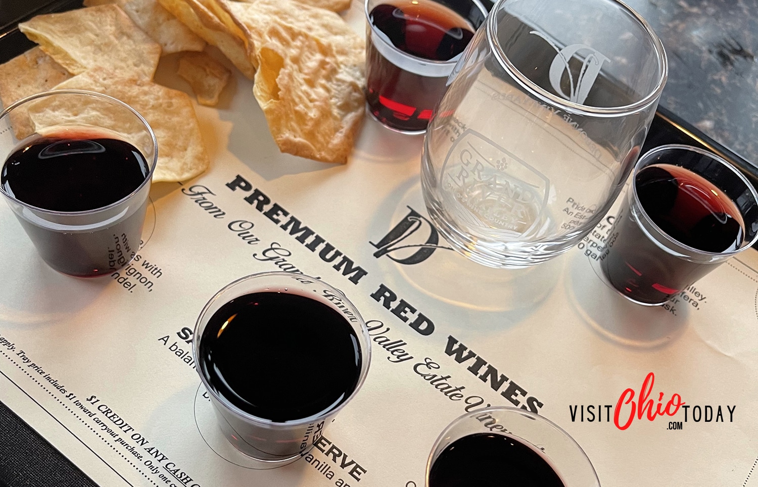 horizontal photo of a flight of red wines on a tray with some chips and a glass at Debonne Vineyards. Photo credit: Cindy Gordon of VisitOhioToday,com