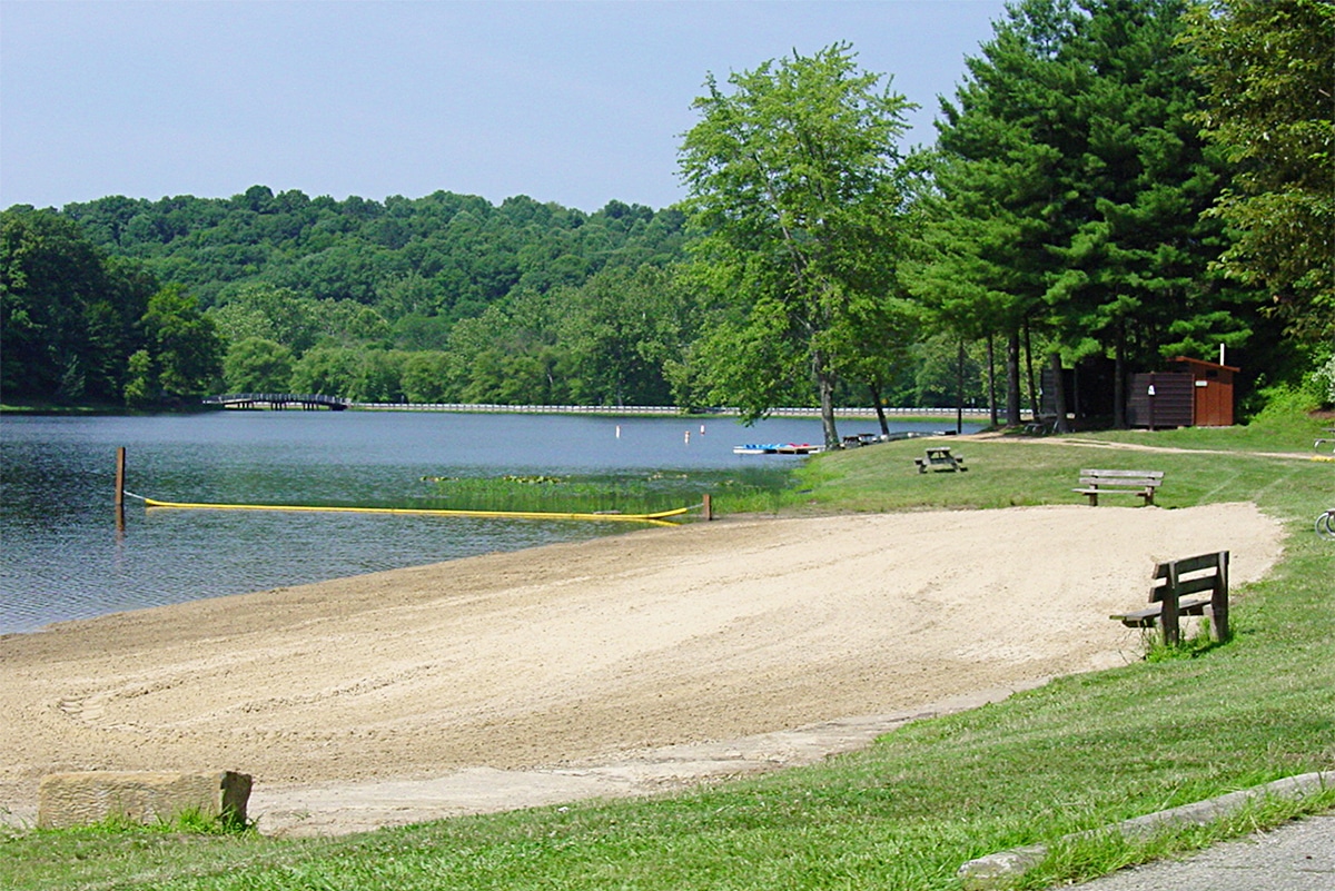horizontal photo of the beach at Lake Alma State Park with boats moored in the distance and trees in the background