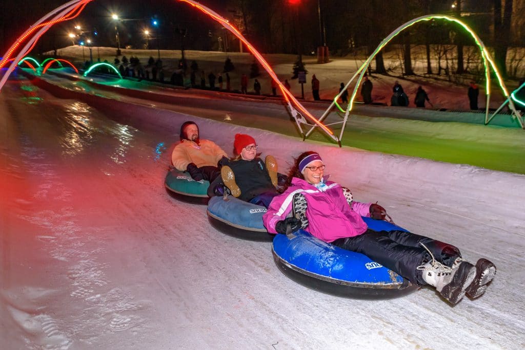 night time, snow tubing slop with glow lights, three people together on three tubes
