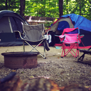 metal rusted firering, two chairs grey and hot pink and two tents in back ground