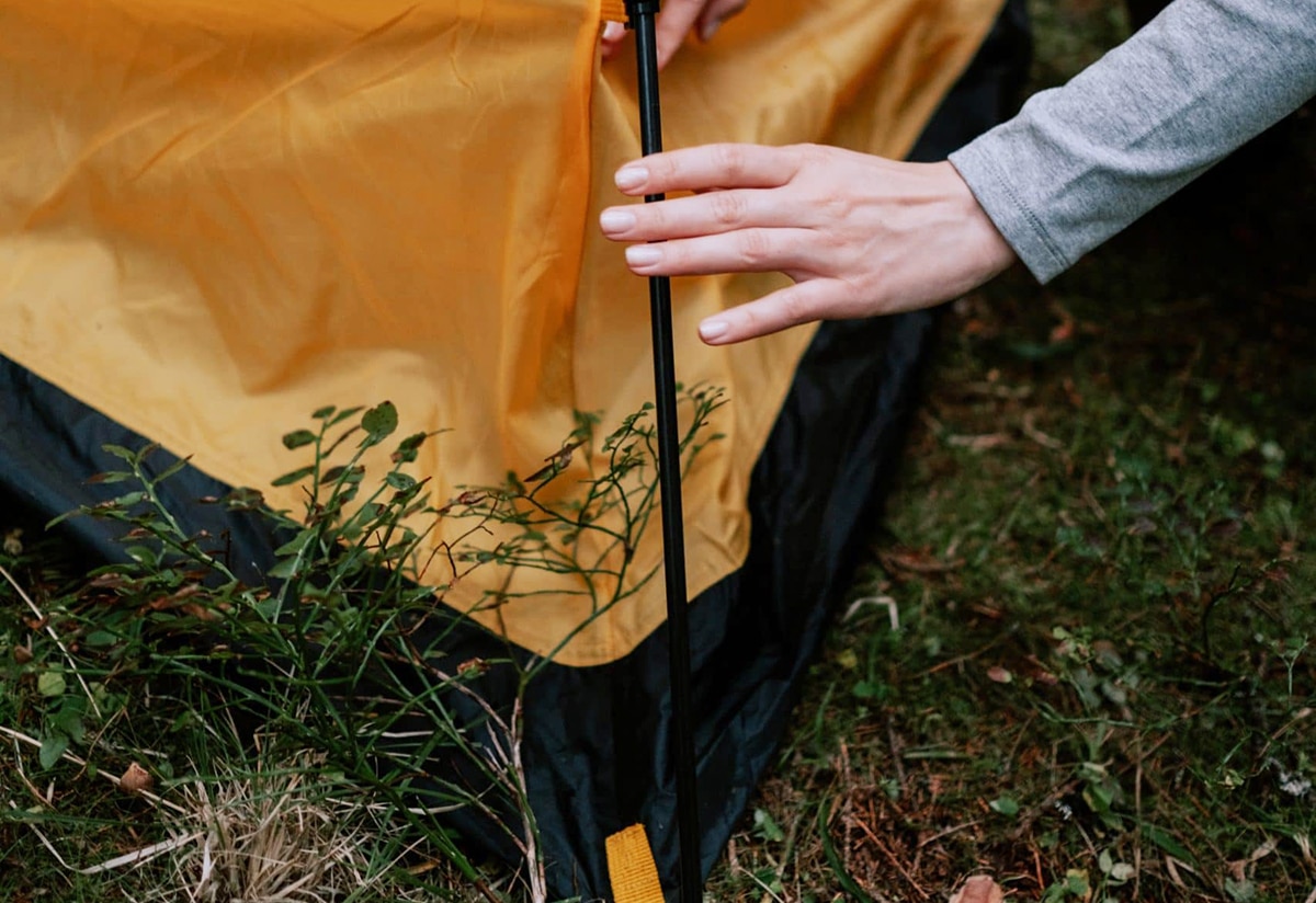 horizontal photo of the corner of a pop-up tent and a woman's hands fixing the pole to the tent