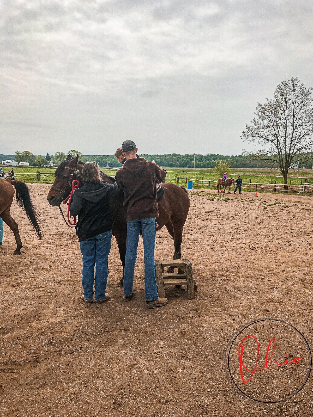 picture of a man and women helping a small child onto a small horse in a dirt arena marmon valley farms