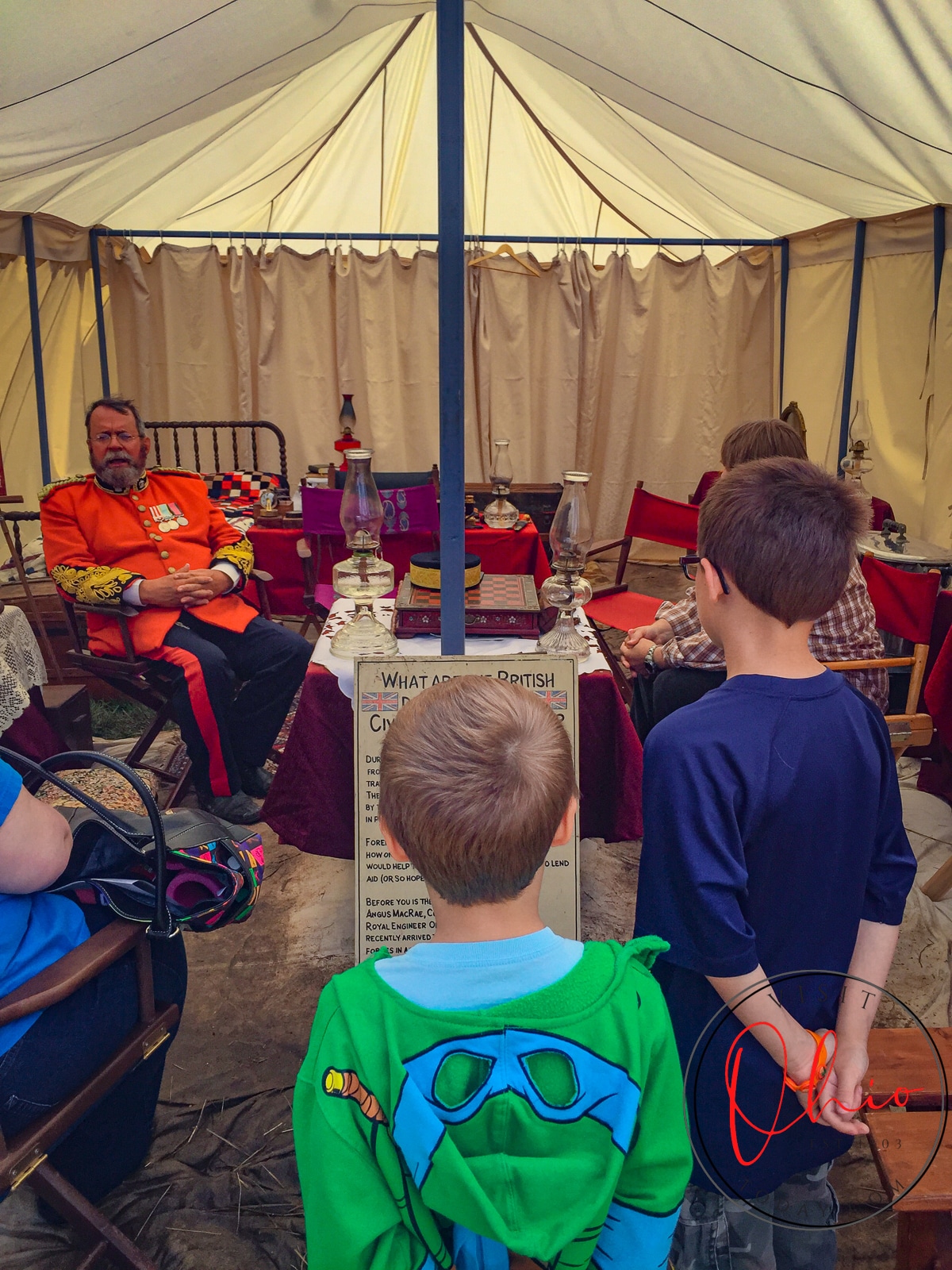 2 young children looking at a man in a red civil war coat in a tent telling a story