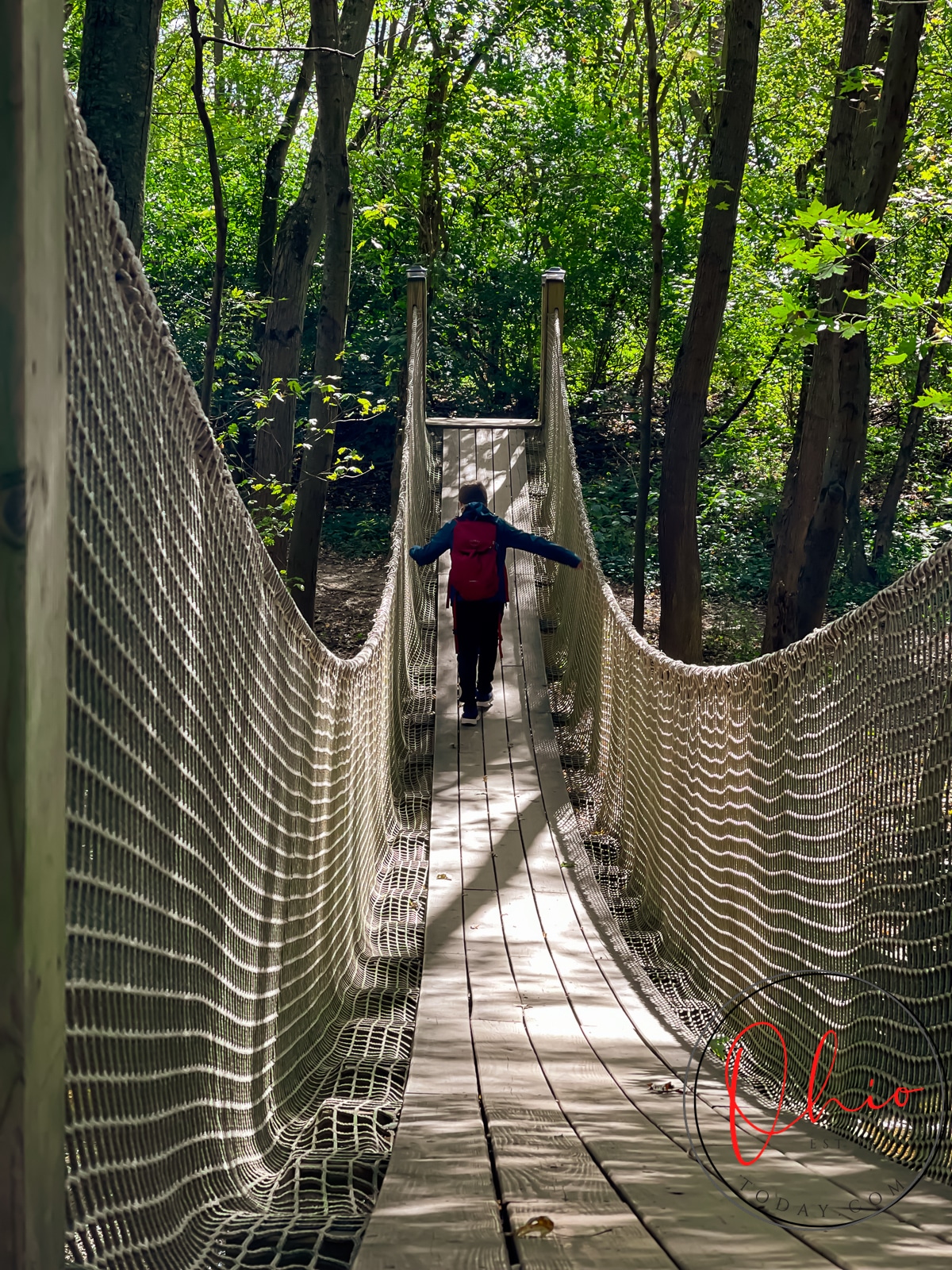 boy in red backpack crossing wooden bridge