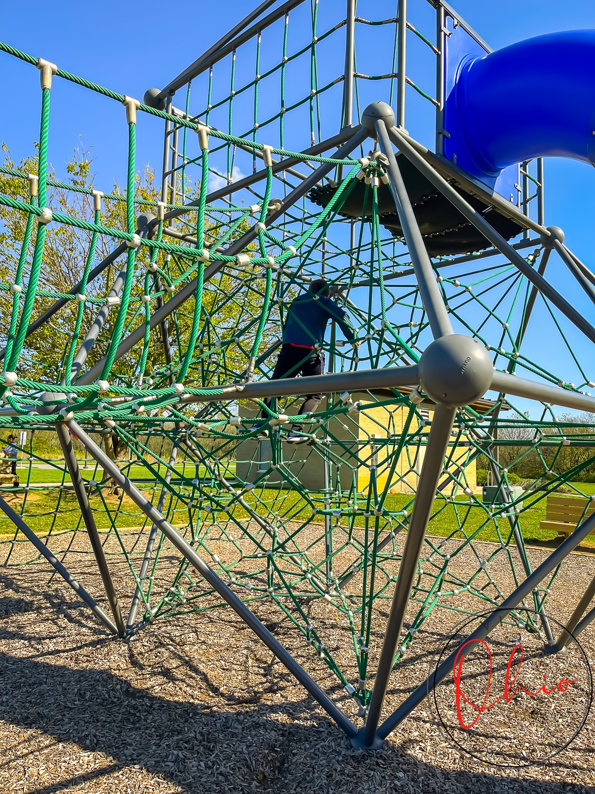 rope course playground with green ropes and brown metal, blue slide, kid crawling up ropes
