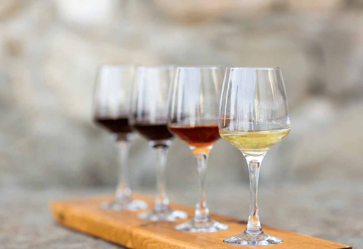 horizontal photo of a flight of wine for tasting with four wines on a wooden stand
