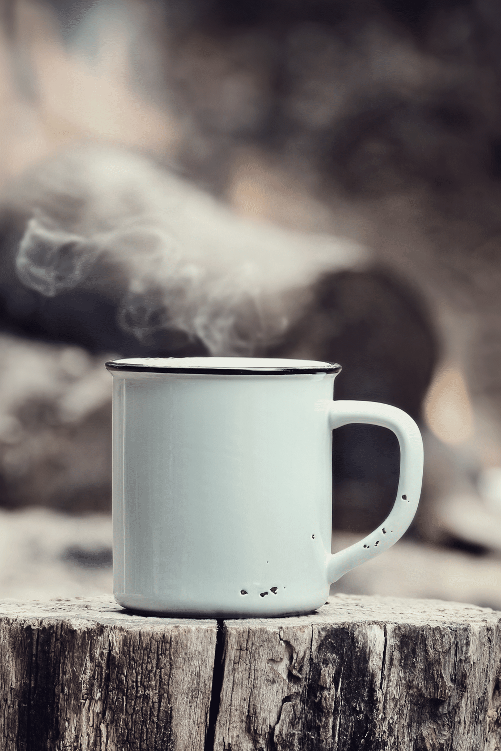 white tin cup of hot steaming liquid on tree stump