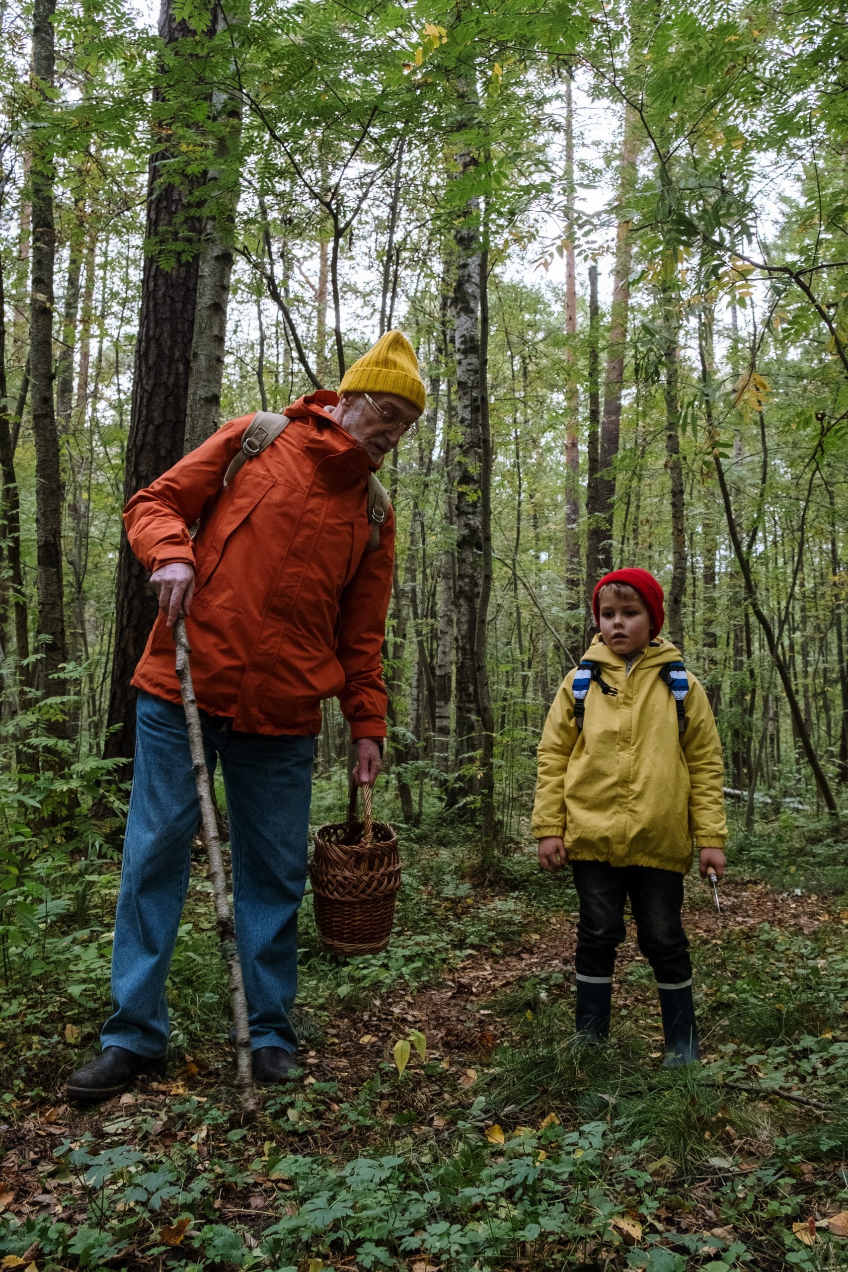 grandpa and young child with hats and rancoats hiking in wooded forest. Looking cold and rainy