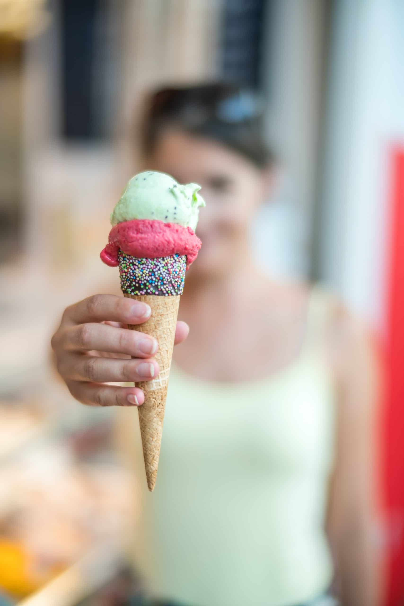 girl in mint green tank top holdnig an ice cream cone of 3 scoops in front of herface