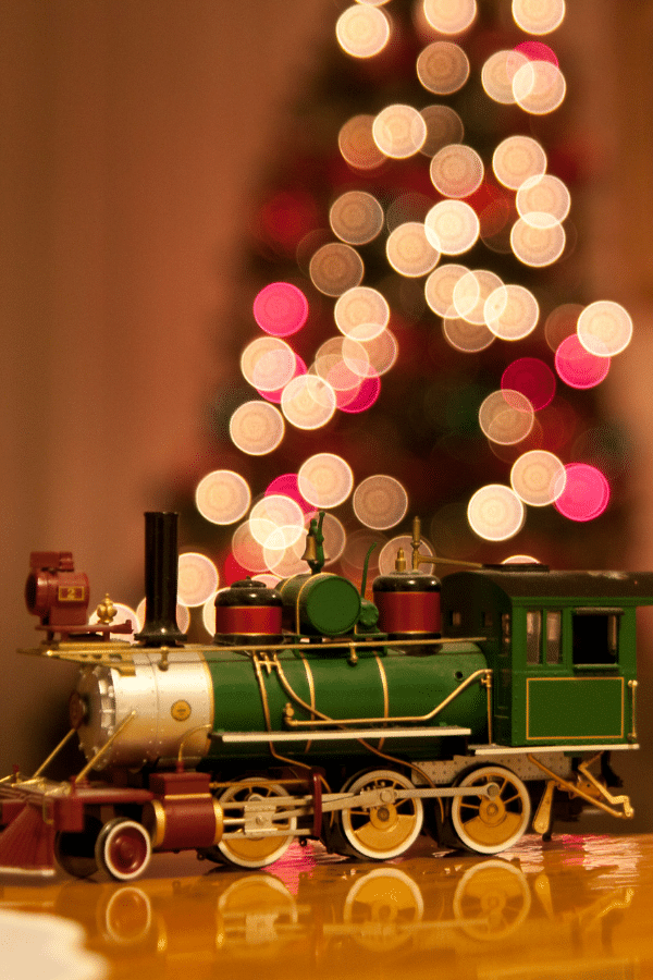 lighted christmas tree in back with green and cold toy train in front of picture