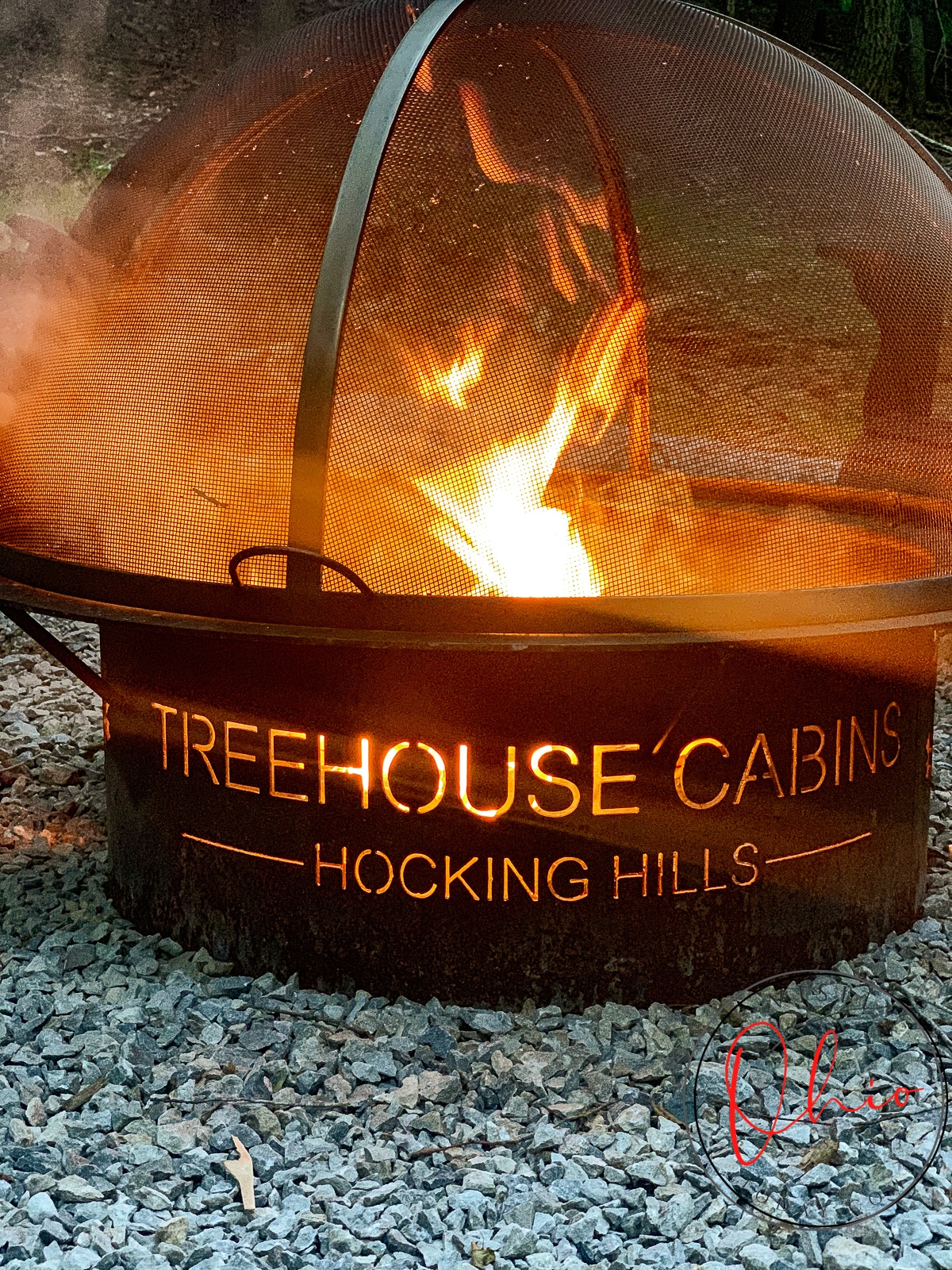 rustic fire pit with cut out words: treehouse cabins and roaring flames in it