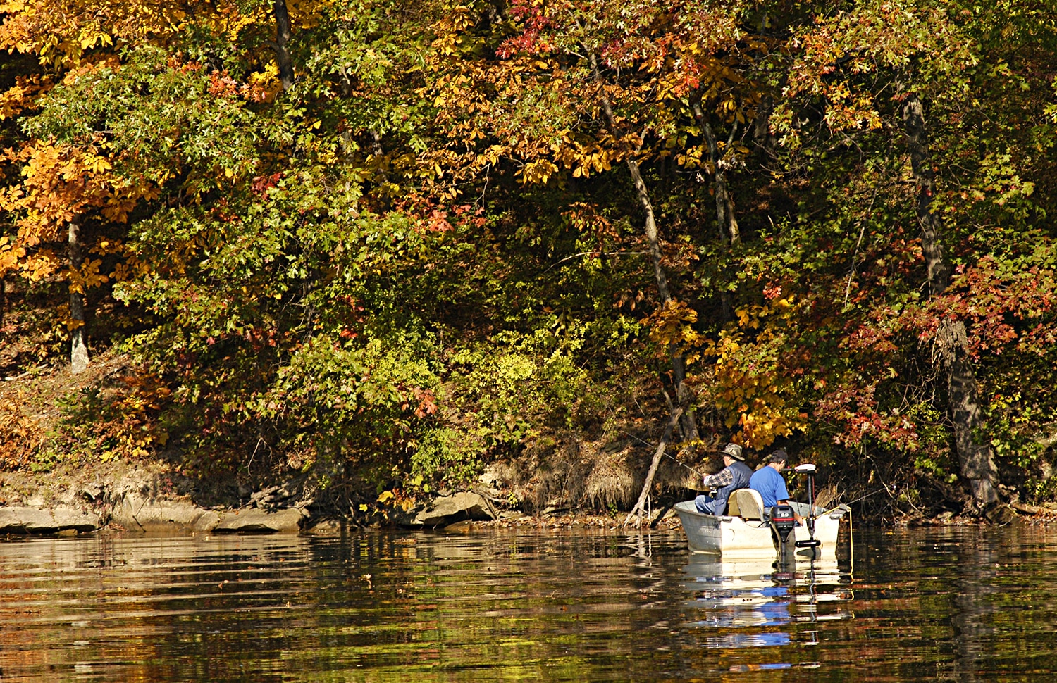 horizontal photo of two men fishing from a boat on the lake at Wolf Run State Park, with lots of fall foliage in the background