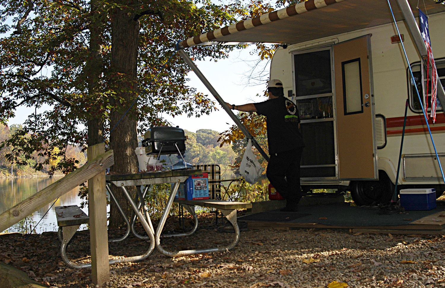 horizontal photo of a man standing outside of his caravan, looking out to the lake at Wolf Run State Park