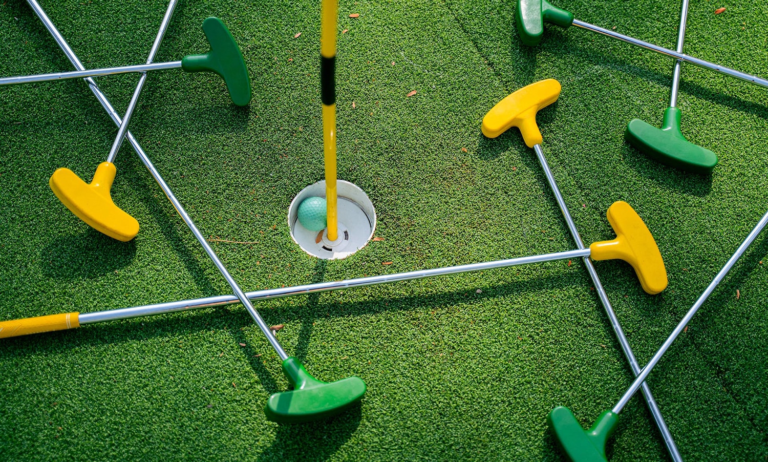 horizontal photo of mini golf clubs on a green with a ball in the hole