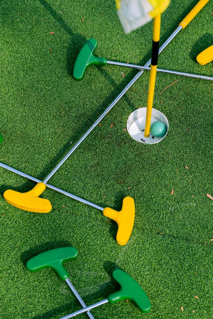 green fake turf at mini golf center with green ball in white up with yellow flag pole. 2 yellow head putters and 2 green head putts randomly thrown on ground Things to do in Youngstown Ohio