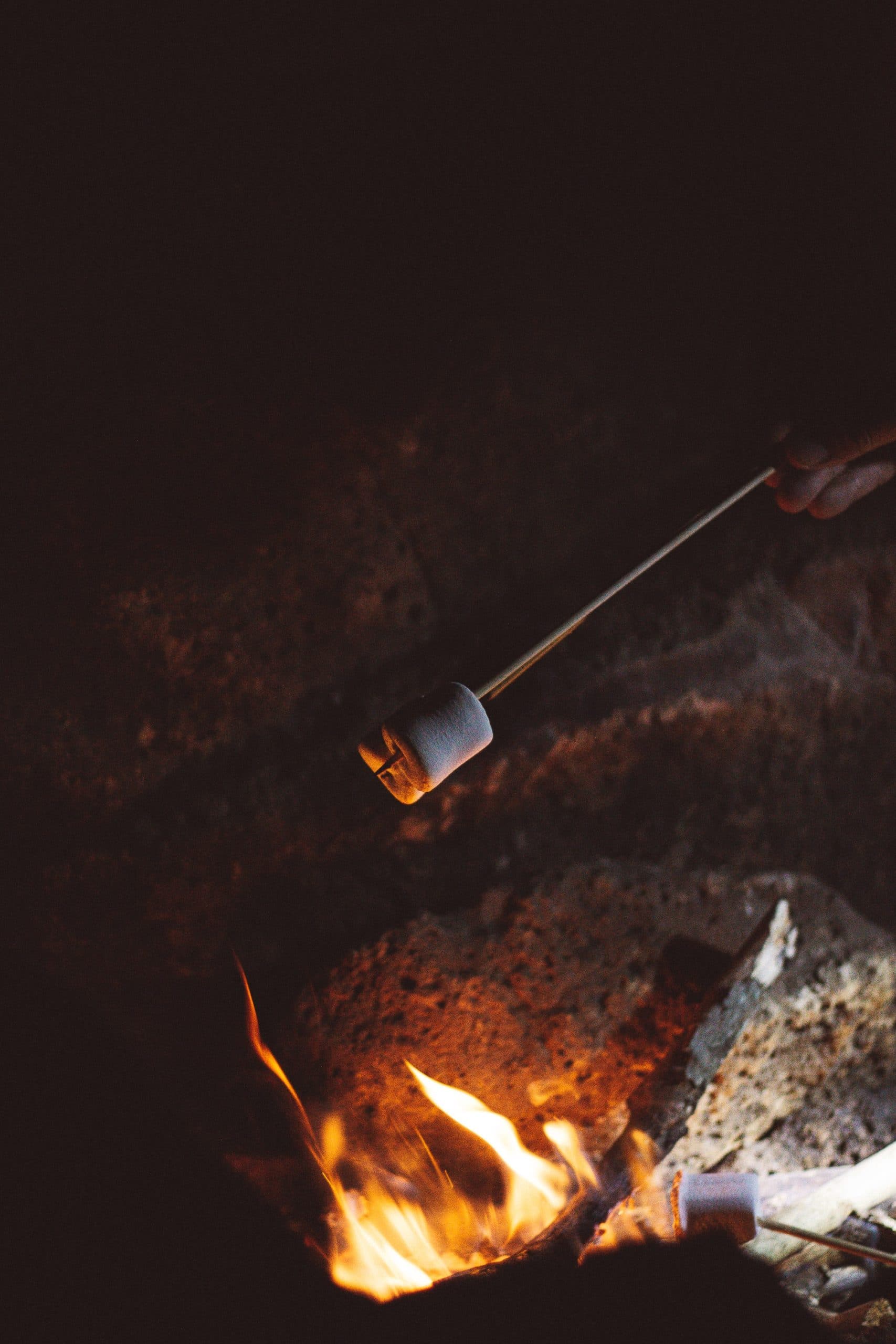 orange flames of bonfire with white half roasted marshmallow on stick over fire