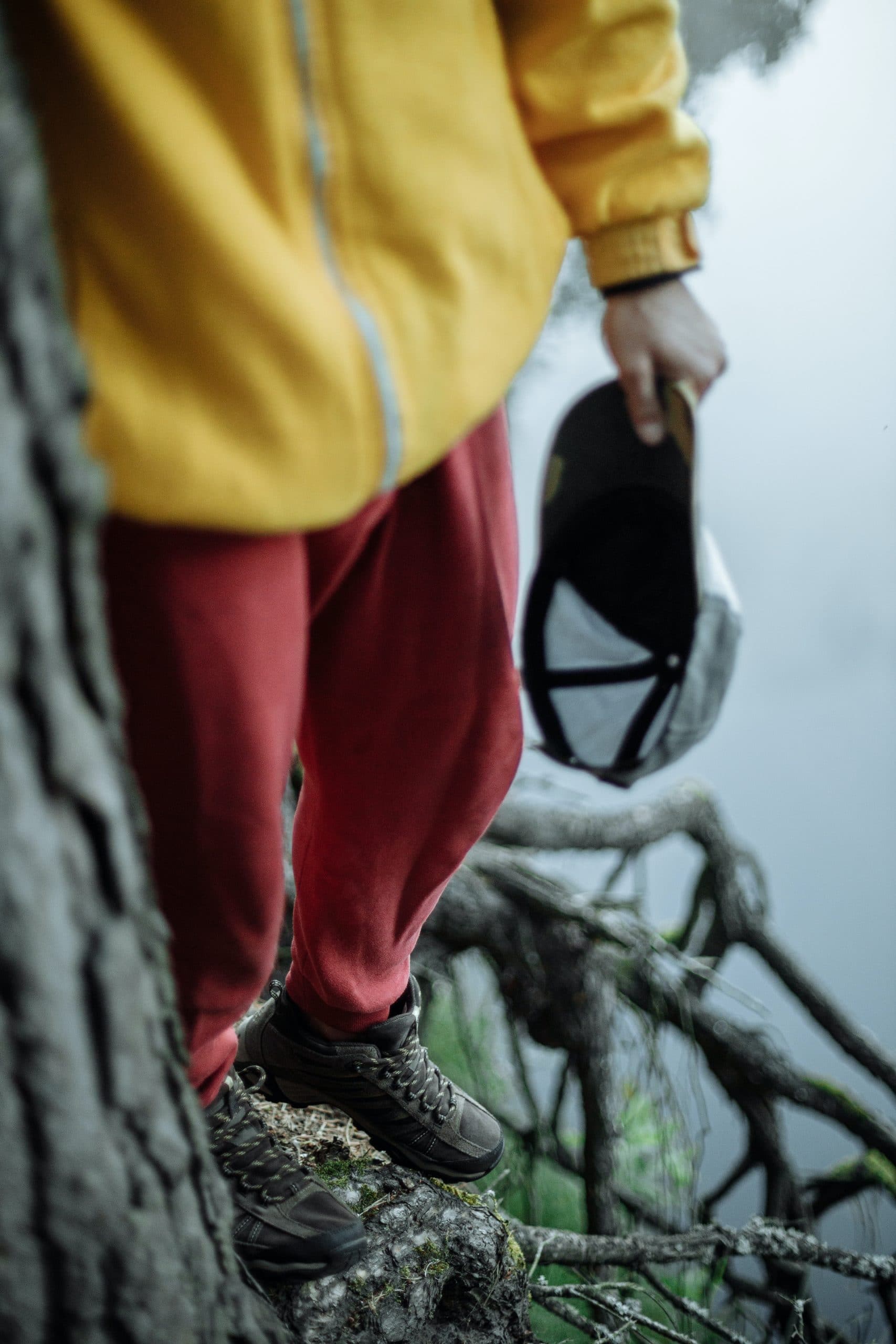 close up shot of young child with yellow sweetshirt and red sweat pants hold a hand and walking on a tree root next to a lake