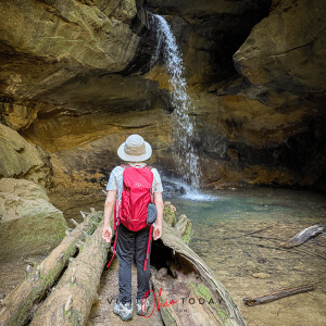 man with hat and red backpack facing a rocking waterfall