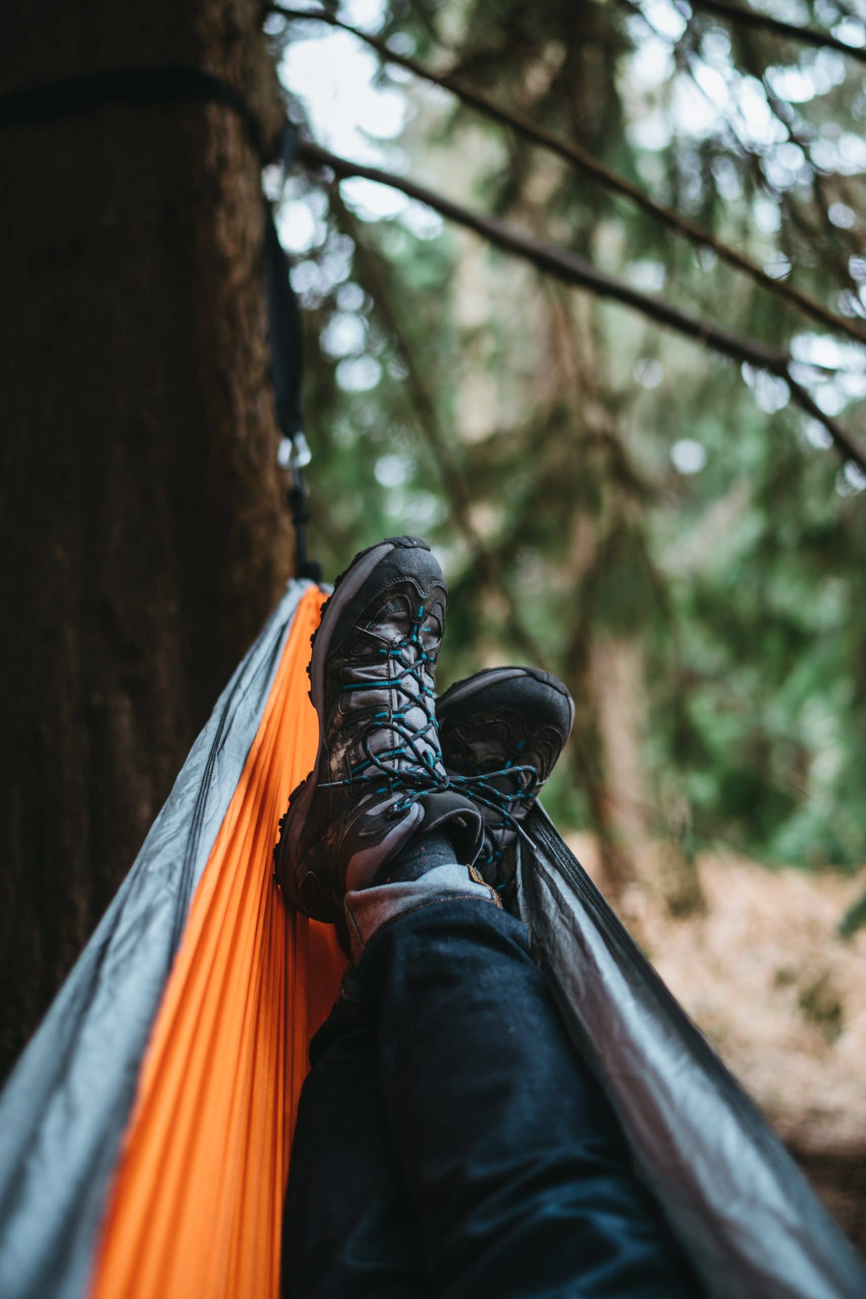 vertical picture of black pants with black hiking boots laying in a hammock in a pine tree