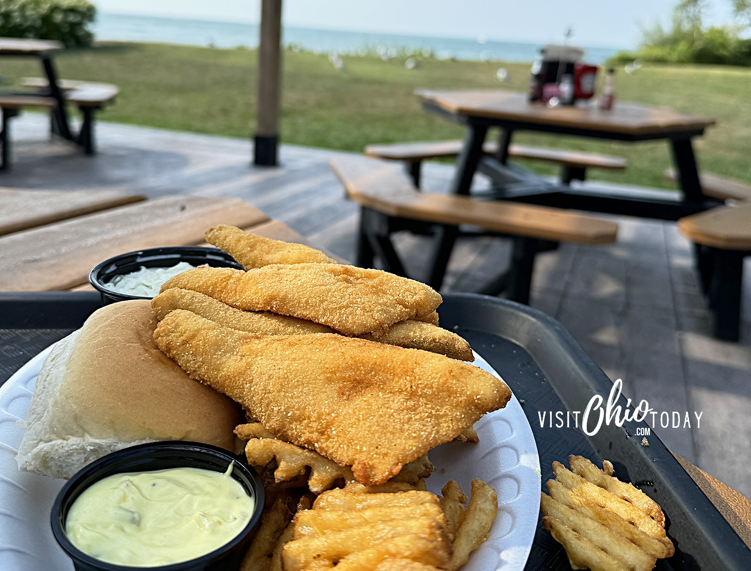 horizontal photo of a plate of fish and fries from Jolly Roger's Seafood House, with a view of Lake Erie in the background. Photo credit: Cindy Gordon of VisitOhioToday.com