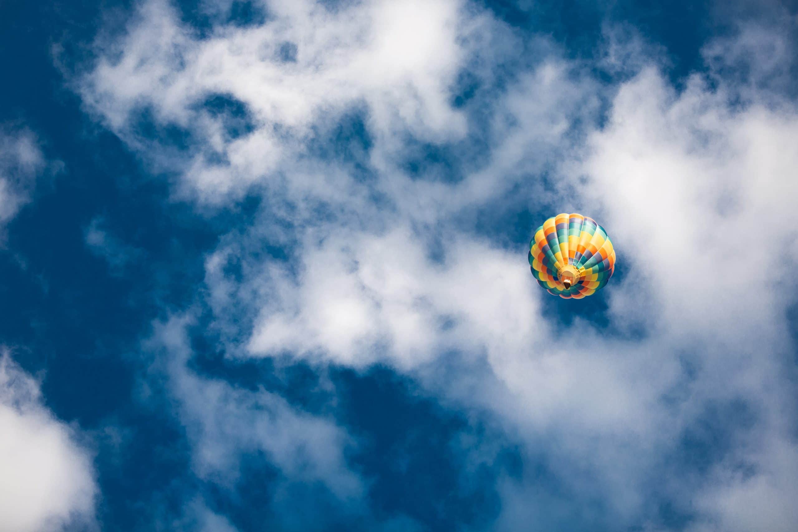 Blue sky with white clouds and a single hot air balloon in flight