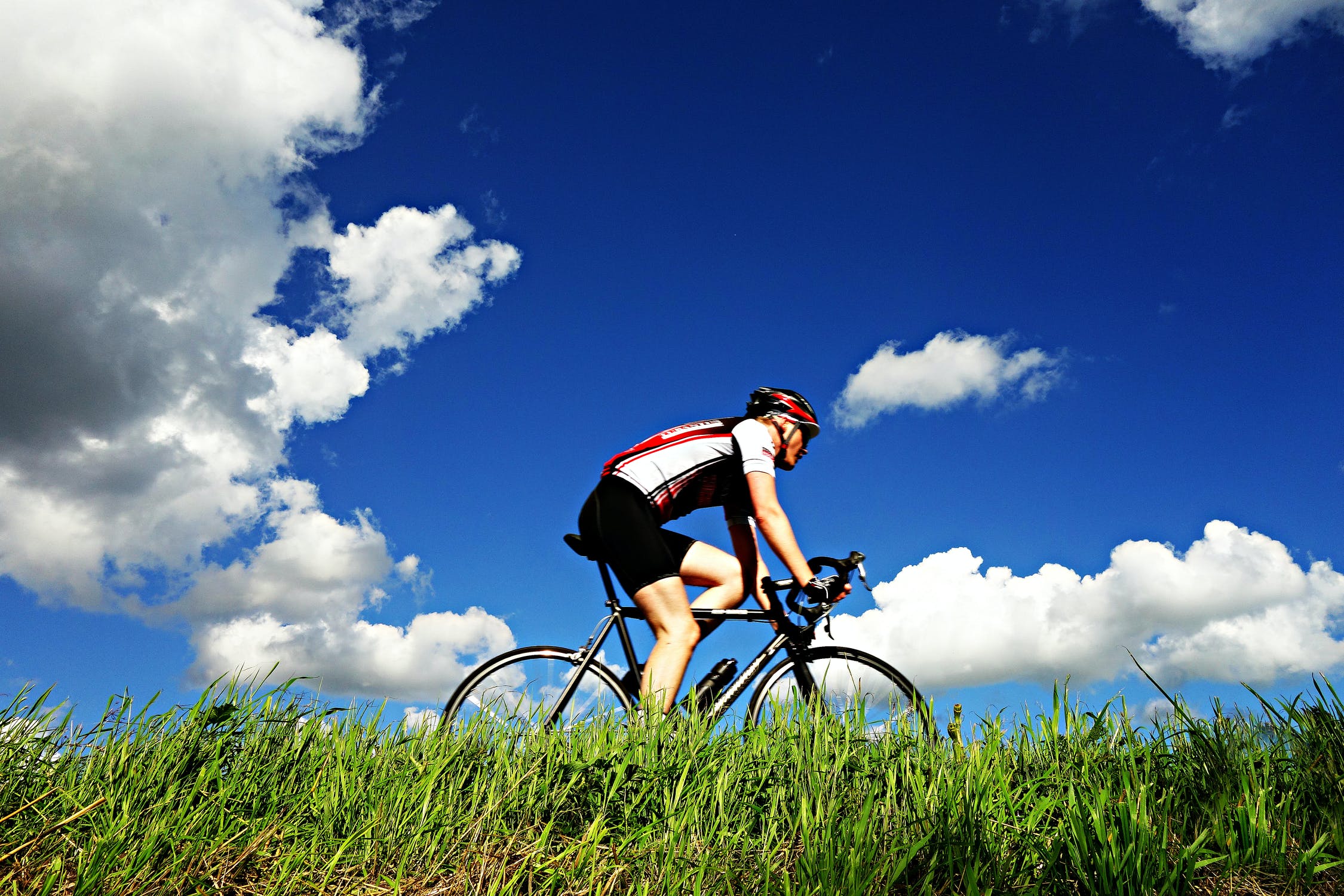 Blue sky with white clouds. A cyclist is riding on green grass