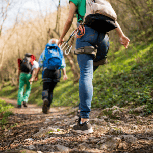 three hikers with gear clipped to them for rock climbing walking on a dirt path