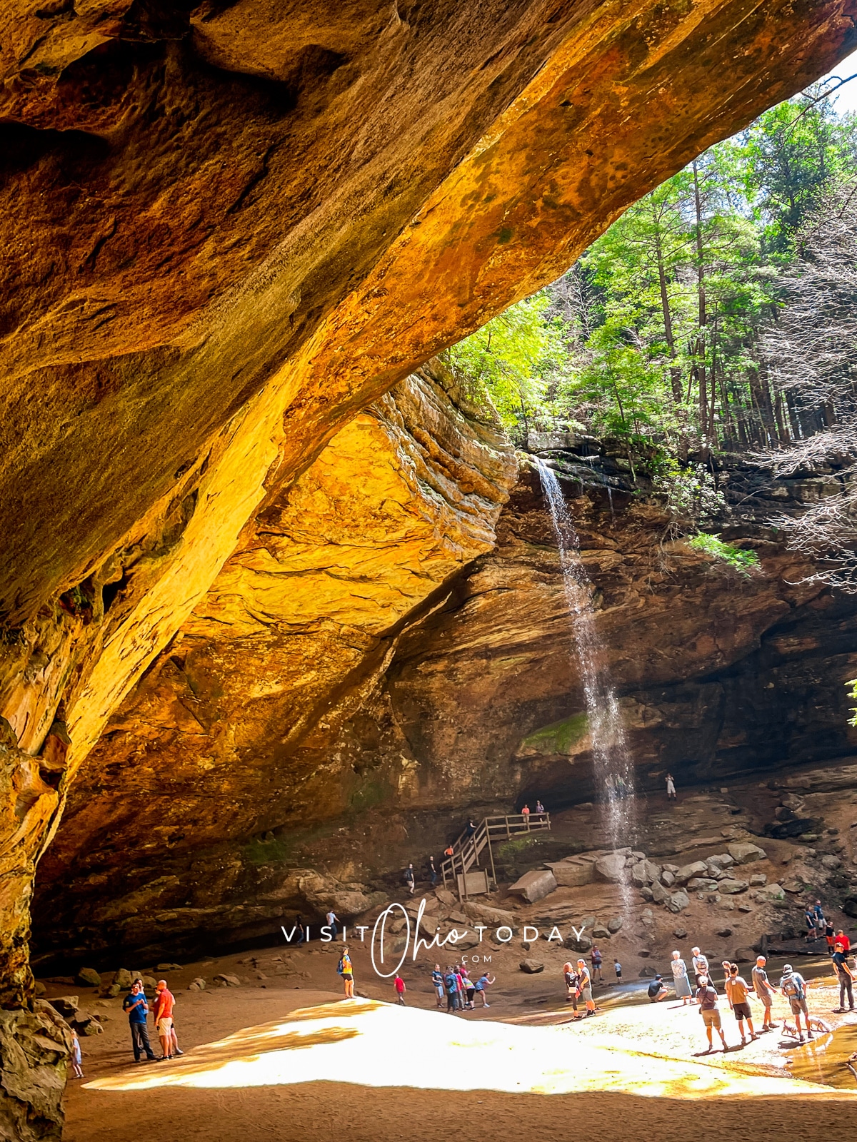 brown cave with tall water fall on right hand side and people walking below the waterfall Photo credit: Cindy Gordon of VisitOhioToday.com