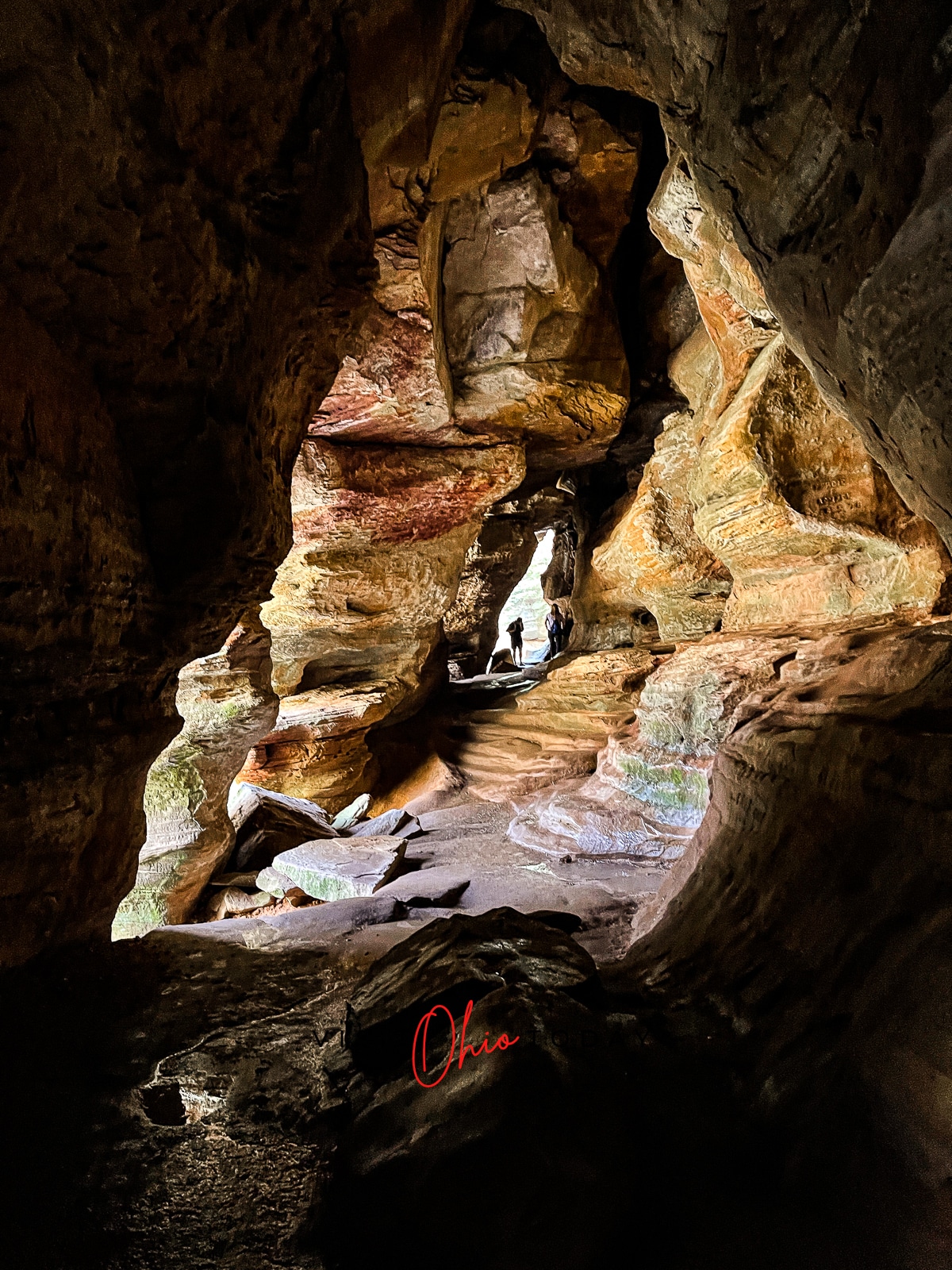 brown rock cave with humans standing at the far end