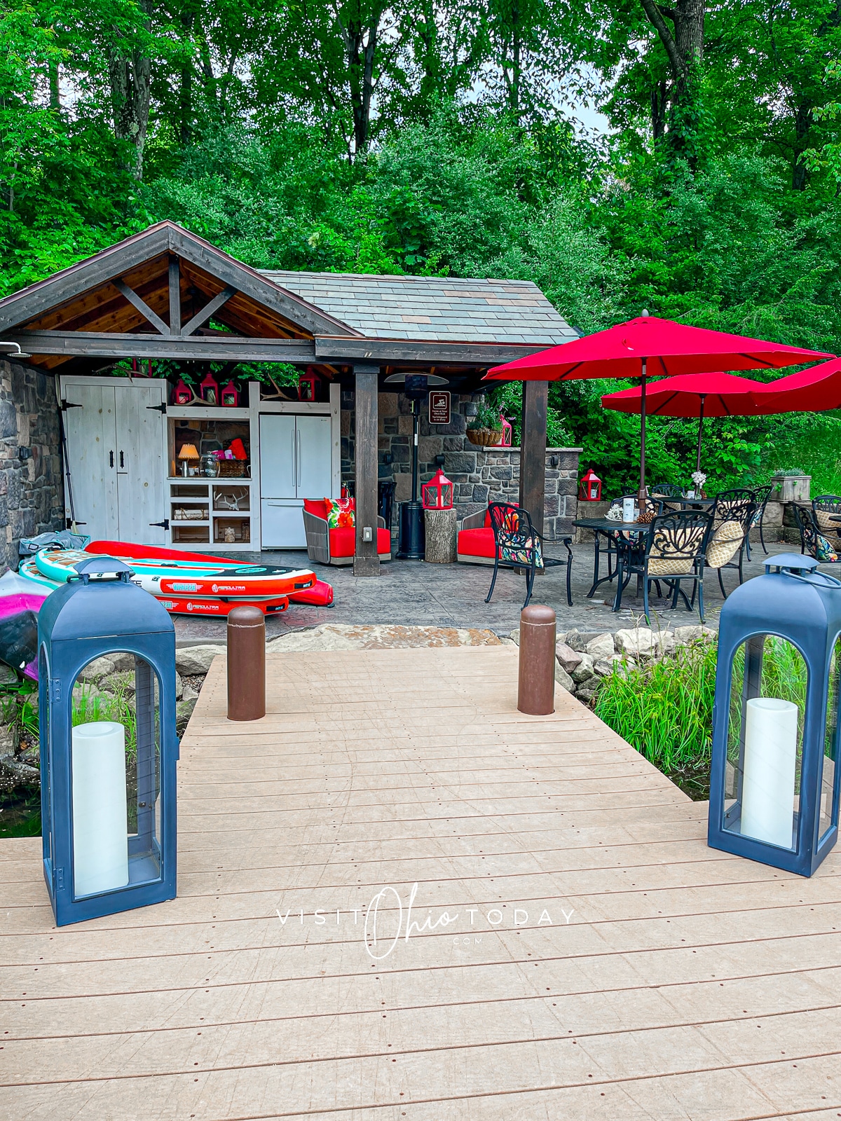 Outside dining area with some paddleboards stacked to the side.The tables have red parasols