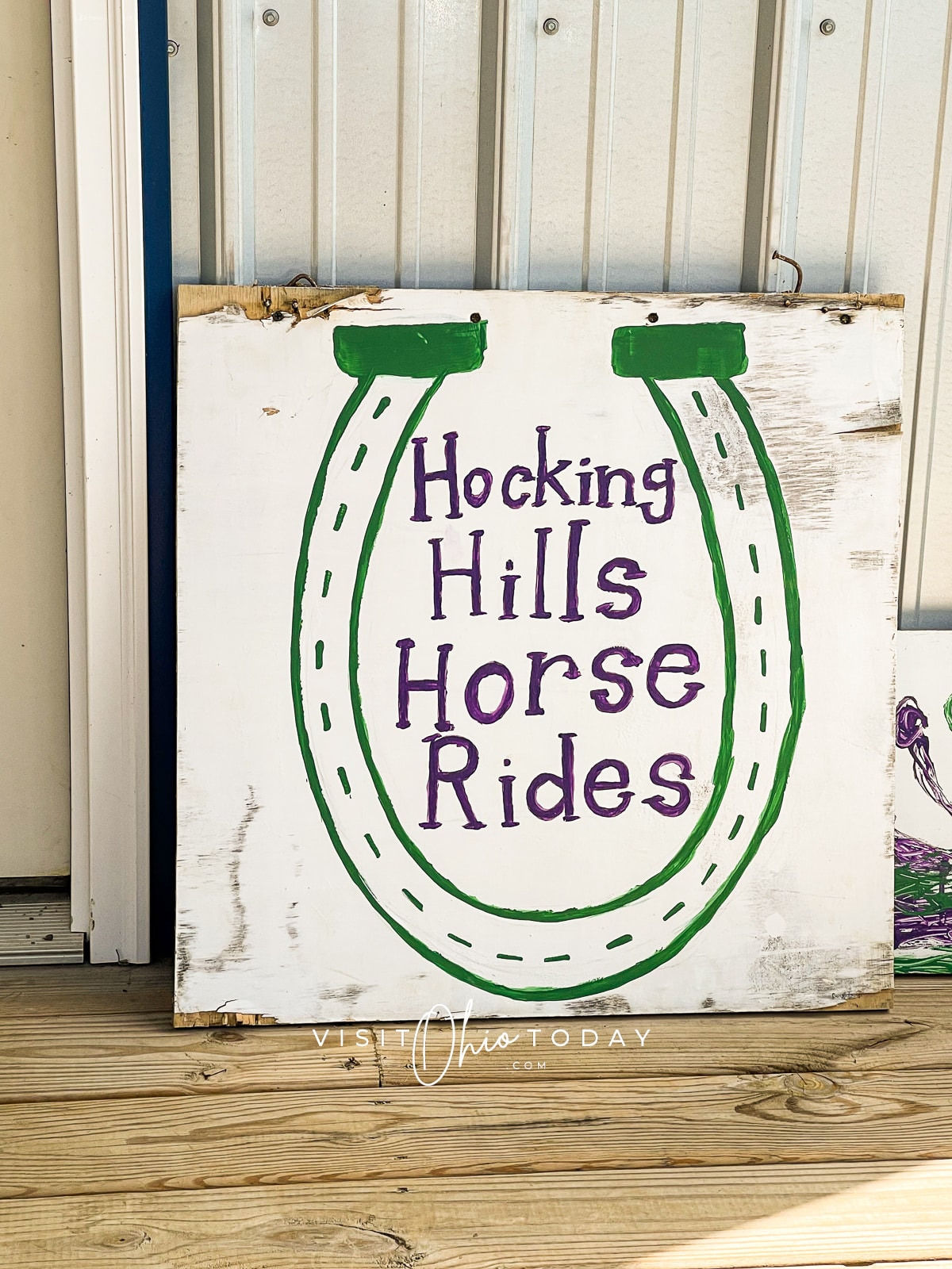 white sign with green horseshoe an words, hocking hills horse rides