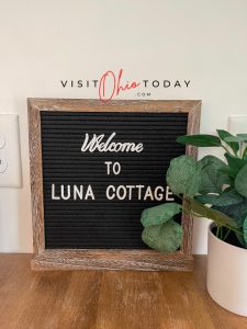 A welcome board that says welcome to luna cottage. A green leafy plant in a cream pot is to the right of the sign