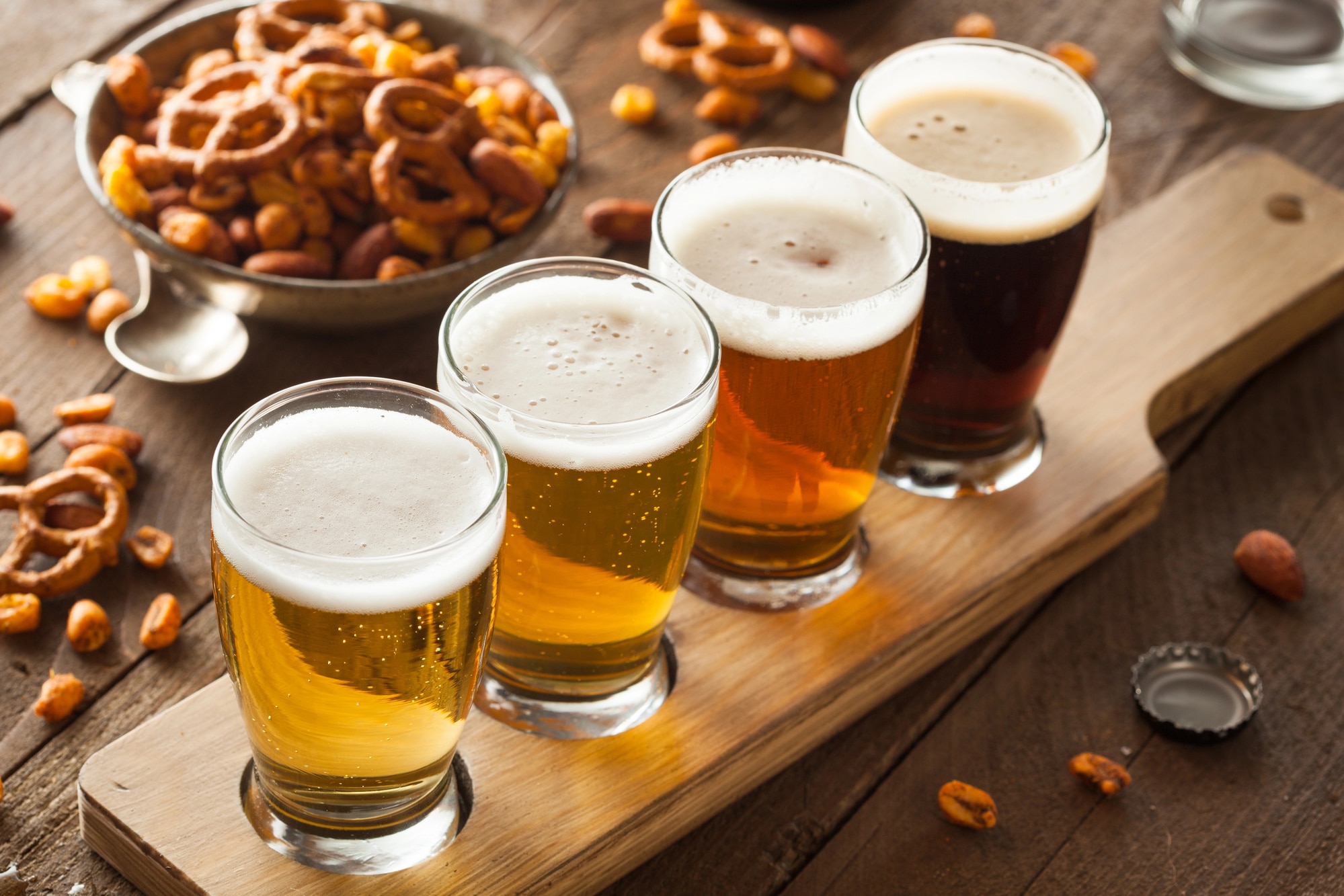 horizontal image of a flight of ales with some snacks in bowls on the table