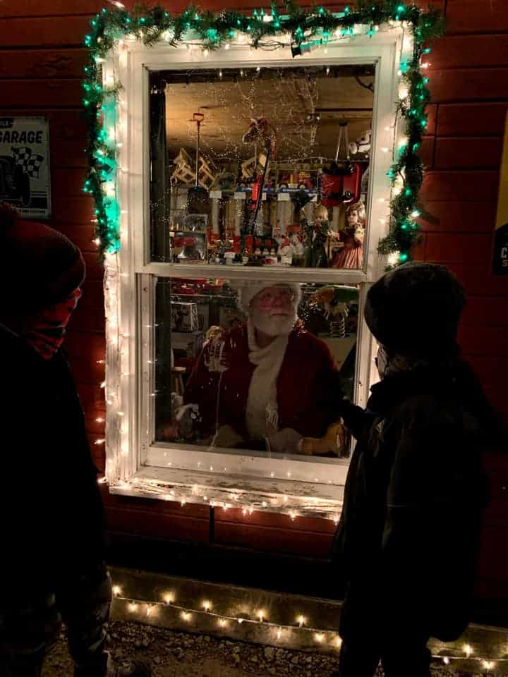 kids peaking into a window with christmas lighst and seeing santa