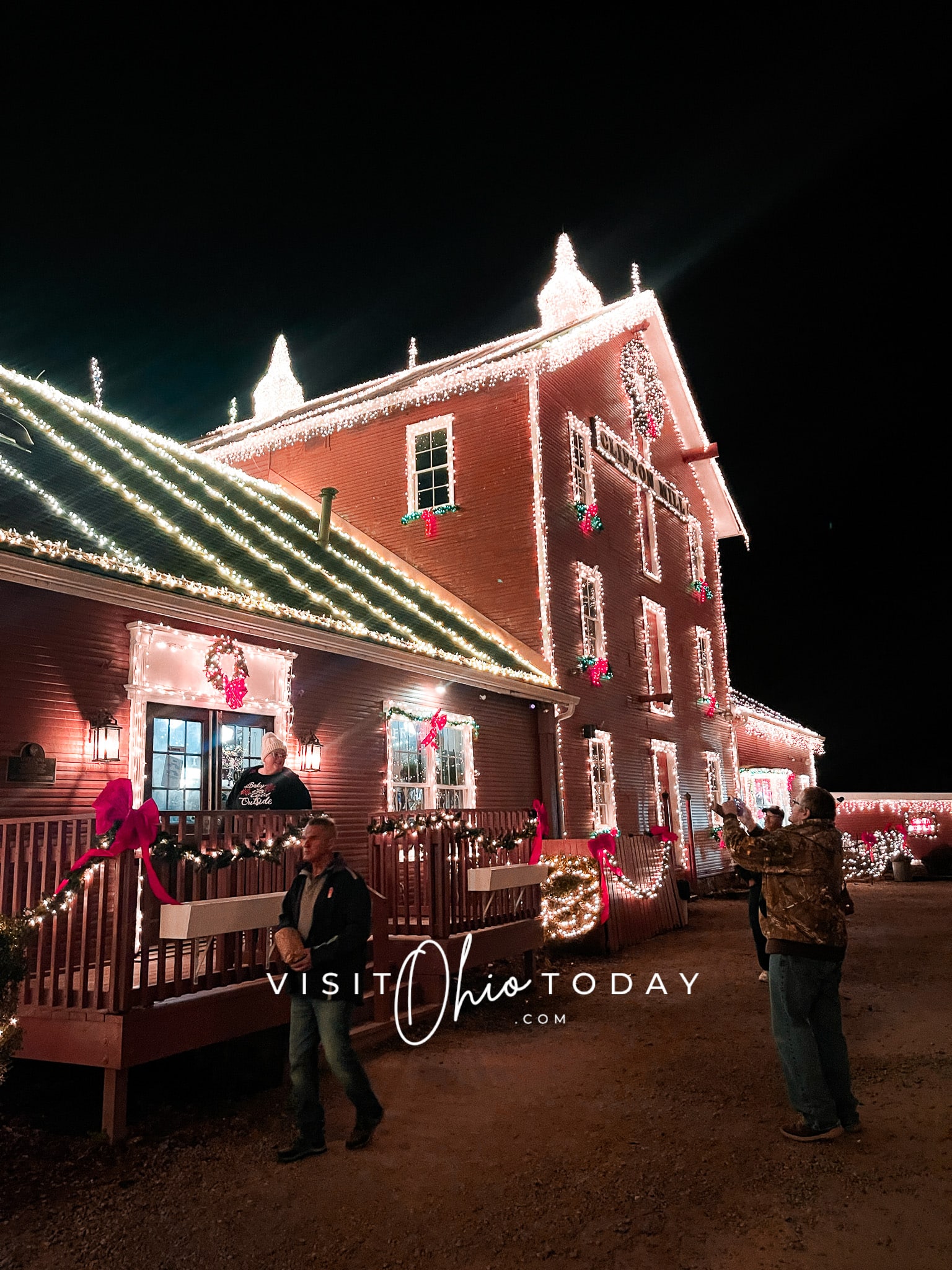 front side of clifton mill decorated with christmas lights, people standing in front taking picture