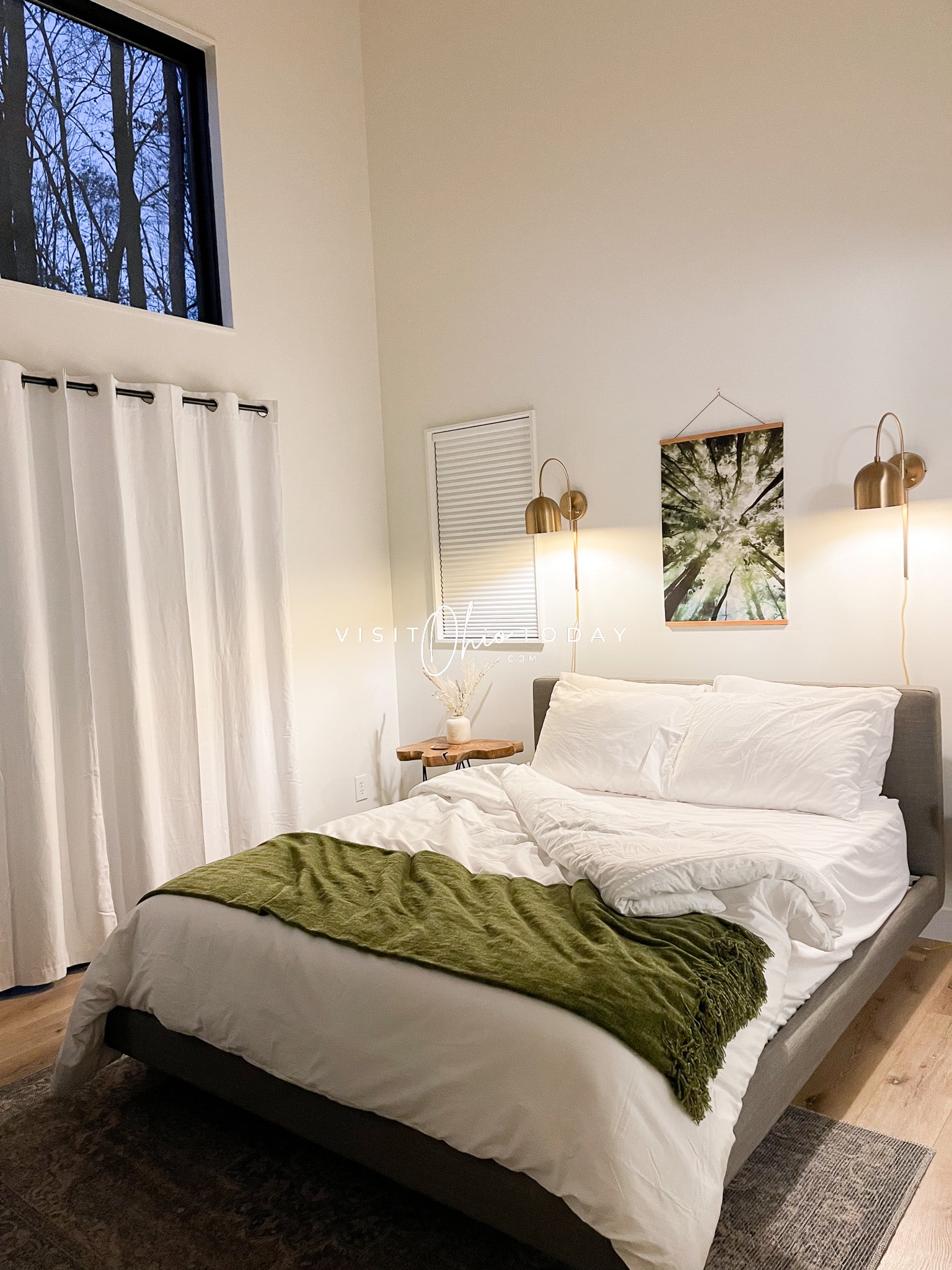 owners suite at ravenhaus, white bed with green blanket folded at end. Pillows on bed, frame on wall, windows have black out shades Photo credit: Cindy Gordon of VisitOhioToday.com