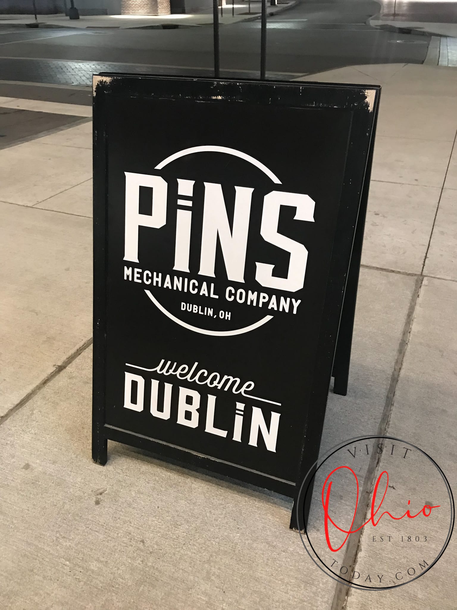 A black sandwich board with the words Pins Mechanical Company Welcome Dublin written in white
