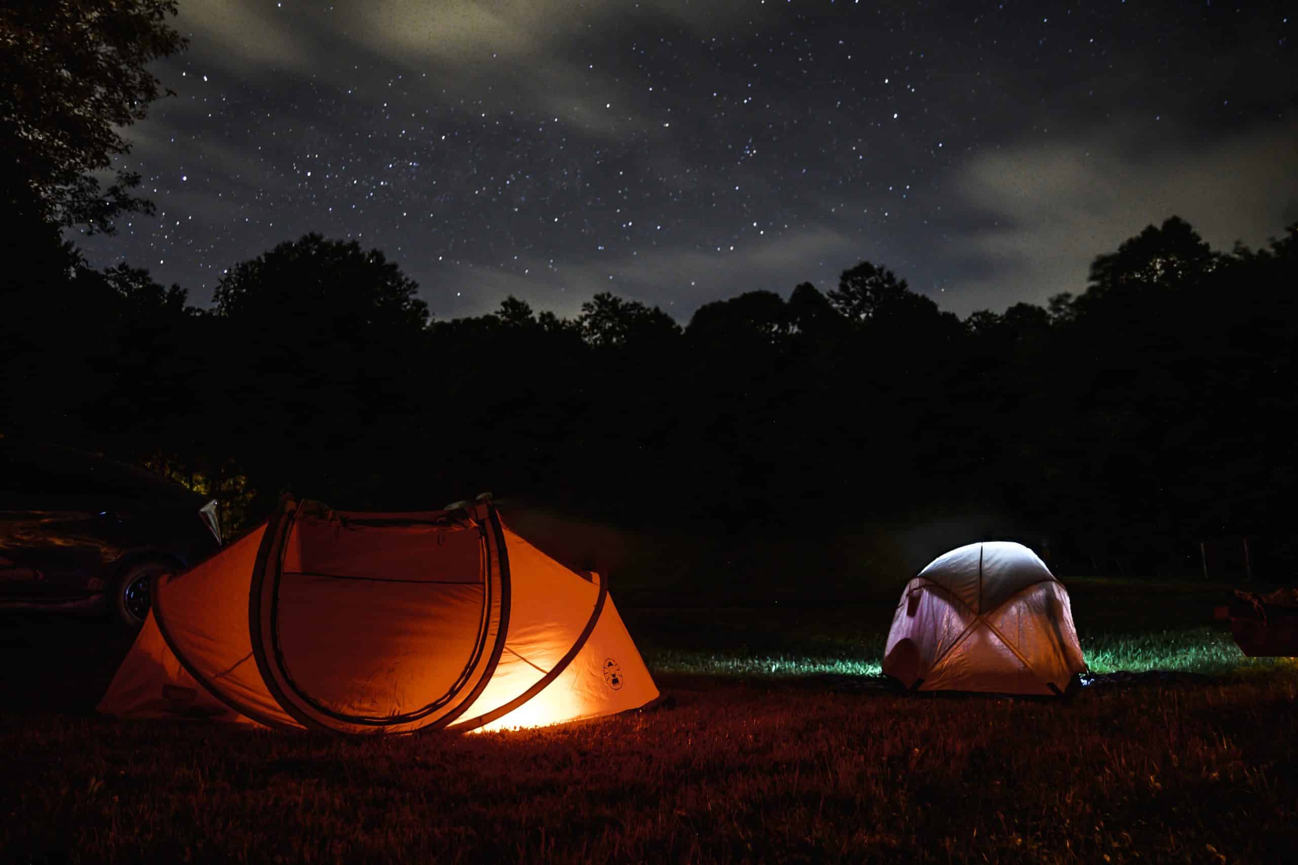 Two lighted tents at night. Above is a starry night sky