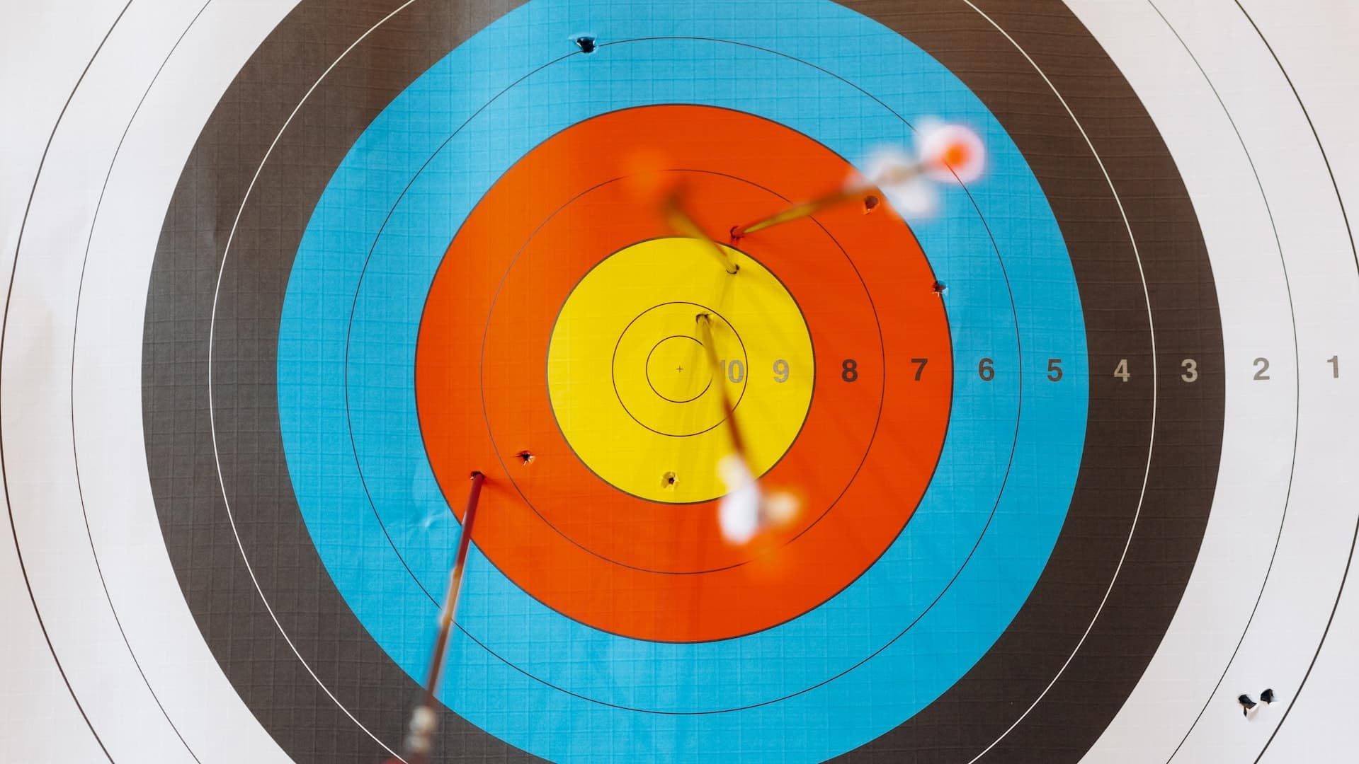 A white, black, blue, red & yellow archery target with arrows shot into it
