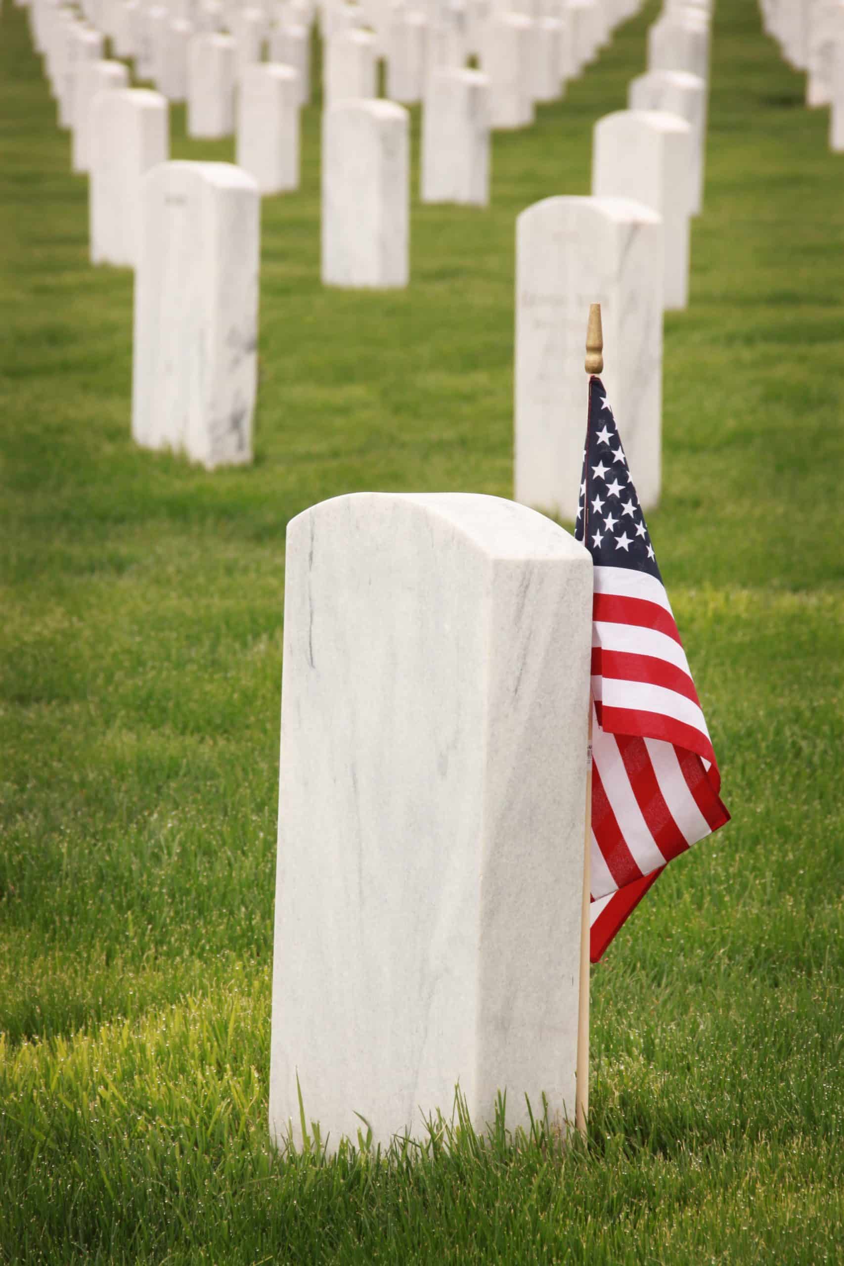 White headstones in a field. One has an American flag of remembrance